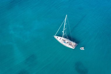 Güneşli bir günde gölde yat. Yelkenli. Deniz yatı, hava fotoğrafçılığı dronu. İnanılmaz bir yat ya da turkuaz ve şeffaf denizi olan bir yelkenli. Mavi göldeki yelkenli teknelerin üst görüntüsü
