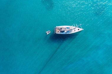 Güneşli bir günde gölde yat. Yelkenli. Deniz yatı, hava fotoğrafçılığı dronu. İnanılmaz bir yat ya da turkuaz ve şeffaf denizi olan bir yelkenli. Mavi göldeki yelkenli teknelerin üst görüntüsü