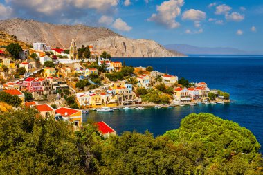 Symi (Simi) ada limanı, klasik gemi yatları, ada tepelerindeki evler, Ege Körfezi manzarası. Yunanistan adaları Rodos adasından tatil turları düzenliyor. Symi, Yunanistan, Dodecanese.