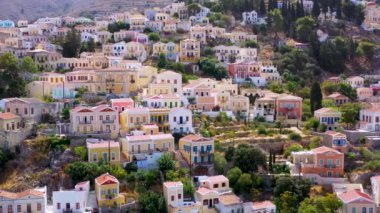 Symi (Simi) ada limanı, klasik gemi yatları, ada tepelerindeki evler, Ege Körfezi manzarası. Yunanistan adaları Rodos adasından tatil turları düzenliyor. Symi, Yunanistan, Dodecanese.