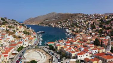 Symi (Simi) ada limanı, klasik gemi yatları, ada tepelerindeki evler, Ege Körfezi manzarası. Yunanistan adaları Rodos adasından tatil turları düzenliyor. Symi, Yunanistan, Dodecanese.