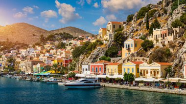 Symi (Simi) ada limanı, klasik gemi yatları, ada tepelerindeki evler, Ege Körfezi manzarası. Yunanistan adaları Rodos adasından tatil turları düzenliyor. Symi, Yunanistan, Dodecanese.