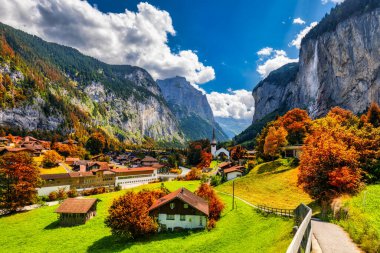 Gün batımında muhteşem Staubbach şelalesi ve İsviçre Alpleri ile Lauterbrunnen Vadisi 'nin büyüleyici sonbahar manzarası. Sonbahar kırmızı yapraklı Lauterbrunnen köyü, Berner Oberland, İsviçre, Avrupa.