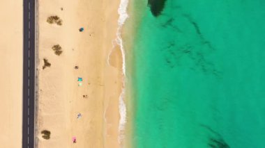 Fuerteventura Adası, İspanya, Kanarya Adaları 'nda turkuaz suyu olan bir sahil. Kum plajının havadan görünüşü, okyanus dokusunun arka plan döngüsü, İHA ile deniz dalgalarının yukarıdan aşağı görüntüsü. Fuerteventura, İspanya.