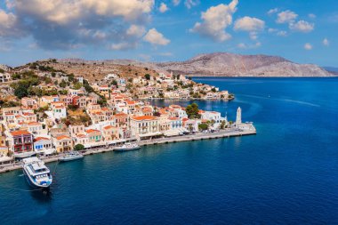 Symi (Simi) ada limanı, klasik gemi yatları, ada tepelerindeki evler, Ege Körfezi manzarası. Yunanistan adaları Rodos adasından tatil turları düzenliyor. Symi, Yunanistan, Dodecanese.