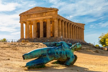 Bronze statue of Icarus in front of the Temple of Concordia at the Valley of the Temples. Temple of Concordia and the statue of Fallen Icarus, in the Valley of the Temples, Agrigento, Sicily, Italy. clipart