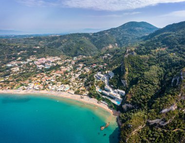 Yunanistan 'ın Korfu adasındaki Agios Gordios egzotik plajı. Agios Gordios plajı, Korfu adası, Yunanistan. Agios Gordios plajının panoramik manzarası, kumlu deniz kıyıları, plaj şemsiyeleri ve şezlonglar..