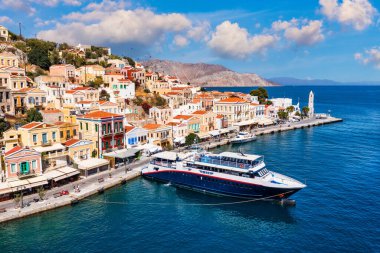 Symi (Simi) ada limanı, klasik gemi yatları, ada tepelerindeki evler, Ege Körfezi manzarası. Yunanistan adaları Rodos adasından tatil turları düzenliyor. Symi, Yunanistan, Dodecanese.