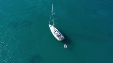 Tropik adanın önündeki kristal berrak turkuaz suya demir atmış, alternatif yaşam tarzı, bir teknede yaşamak. Turkuaz suda demirleyen yatın havadan görünüşü lüks ve zenginliği gösteriyor..