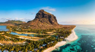 Mauriutius 'taki Le Morne sahilinde palmiye ağaçları ve şemsiyelerle dolu bir plaj. Lüks tropikal plaj ve Mauritius 'taki Le Morne dağı. Palmiye ağaçları, beyaz kumlar ve lüks tatil beldeleri olan Le Morne plajı, Mauritius.
