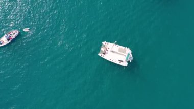 Tropik adanın önündeki kristal berrak turkuaz suya demir atmış, alternatif yaşam tarzı, bir teknede yaşamak. Turkuaz suda demirleyen yatın havadan görünüşü lüks ve zenginliği gösteriyor..