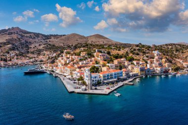 Symi (Simi) ada limanı, klasik gemi yatları, ada tepelerindeki evler, Ege Körfezi manzarası. Yunanistan adaları Rodos adasından tatil turları düzenliyor. Symi, Yunanistan, Dodecanese.