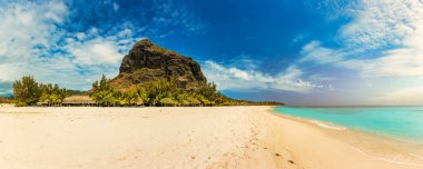 A beach with palm trees and umbrellas on Le morne Brabant beach in Mauriutius. Tropical crystal ocean with Le Morne beach and luxury beach in Mauritius. Le Morne beach with palm trees, white sand and luxury resorts, Mauritius. clipart