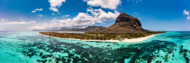 Mauriutius 'taki Le Morne sahilinde palmiye ağaçları ve şemsiyelerle dolu bir plaj. Lüks tropikal plaj ve Mauritius 'taki Le Morne dağı. Palmiye ağaçları, beyaz kumlar ve lüks tatil beldeleri olan Le Morne plajı, Mauritius.