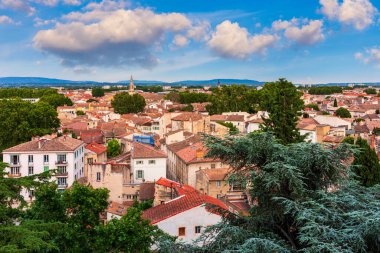 Avignon 'un pitoresk kasabası, Fransa' nın Avignon şehrinde sakin bir atmosfer yaratan, parlak mavi gökyüzü altında kırmızı çatıları ve yemyeşil yeşillikleri olan tarihi binaların bir karışımını ortaya koyuyor..