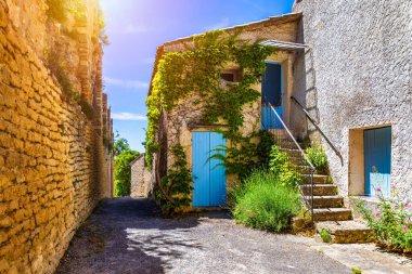 Venasque 'da güneş taşı ve canlı çiçeklerle dolu büyüleyici dar bir cadde, Provence, Fransa. Venasque 'nin pitoresk köyünde dar bir sokakta canlı çiçeklerle süslenmiş taş binalar var..