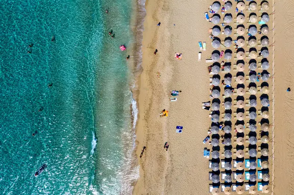 Renkli şemsiyeli kumlu sahil manzarası yazın günbatımında şeffaf mavi suyla deniz koyunda yüzen insanlar. Sahildeki hava manzarası, şemsiyeler, kum ve deniz dalgaları..