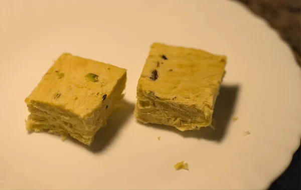 İki parça Hint şekeri, Soan Papdi beyaz bir tabakta servis edildi..