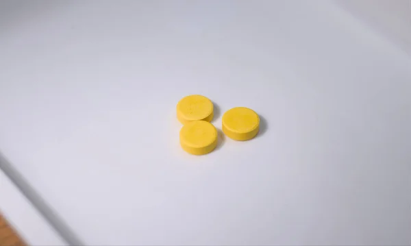 Beyaz bir yüzeye üç sarı hap ya da tablet ilacı. Kapat..