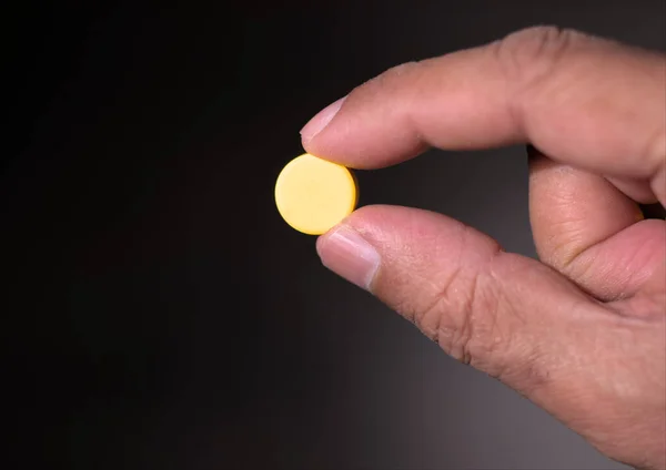 Sarı bir hap ya da iki parmağıyla tablet ilaç tutan bir adam. Kapat..