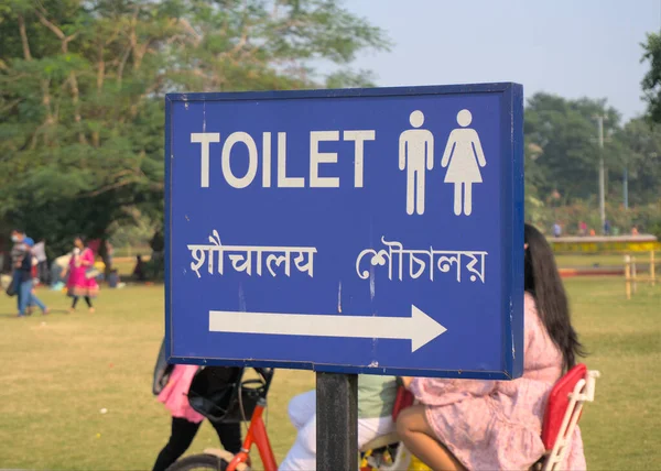 Toilet Direction board written in three languages, English, Hindi and Bengali on a blue signboard.