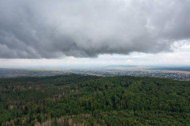 Yoğun çam ormanlarıyla kaplı katmanlı dağ sıralarının ve bulutlu gökyüzünün altındaki vadideki küçük kasabanın çarpıcı manzarası.