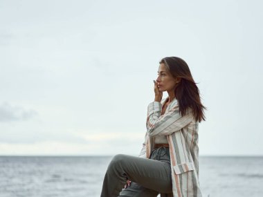 Bulutlu bir günde kıyıda poz veren beyaz beyaz, çekici bir kadın.