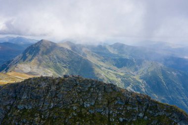 Sersemletici beyaz bulutlar ve mavi gökyüzü katmanlı dağ sıraları ve güneşli bir günde bitki örtüsüyle kaplı vadi üzerinde.