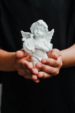 Beyaz açılı bir biblo taşıyan siyah gömlekli ellerin dikey yakın çekimi.