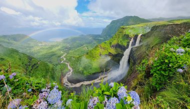Poco do Bacalhau şelalesi ile gökkuşağı kemeri ve Flores Adası 'nda yeşillikle kaplı kayalık dağlar.