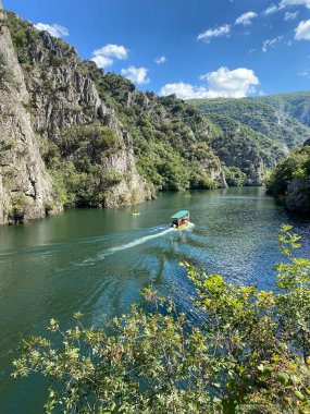 Yeşil kayalıklarla çevrili bir tekneyle nehrin dikey görüntüsü..