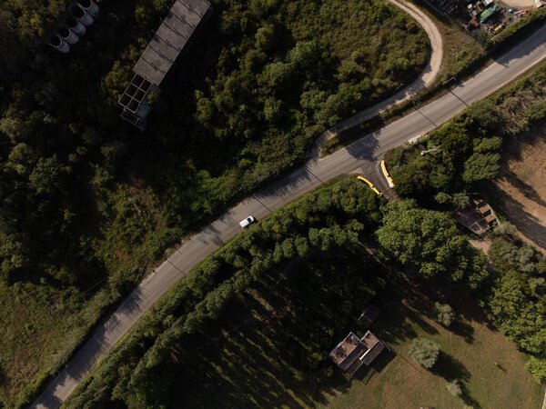 An aerial top view of a single white car on a highway through a green forest in Portugal