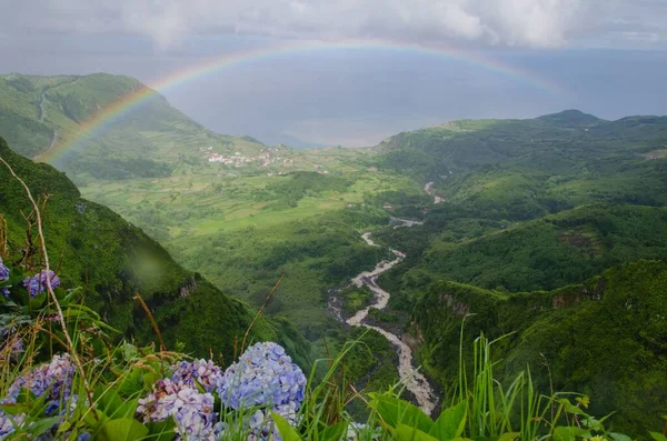 The rainbow arch over the mountains covered with greenery in Flores Island