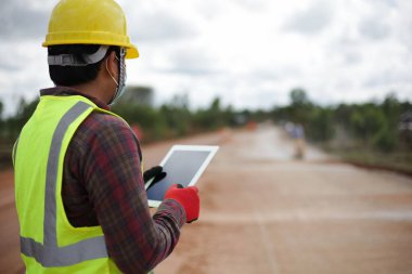 Tabletli kask takan bir erkek müteahhit kırsal beton yol şantiyesinde çalışmayı denetliyor..