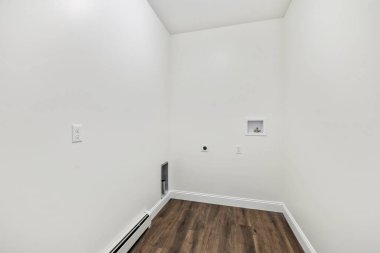 Parke zemini olan bir odanın içi, beyaz duvarlarda elektrik prizleri ve süpürgelik ısıtıcısı olan.