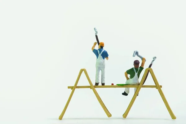 The miniature figures of construction workers painting the walls on a white background