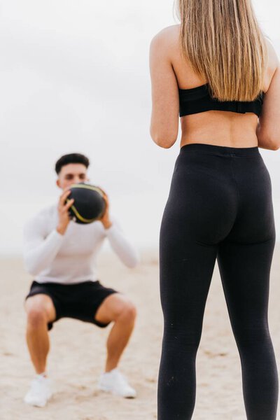 A young athletic couple exercising at the beach, doing squats with gym equipment