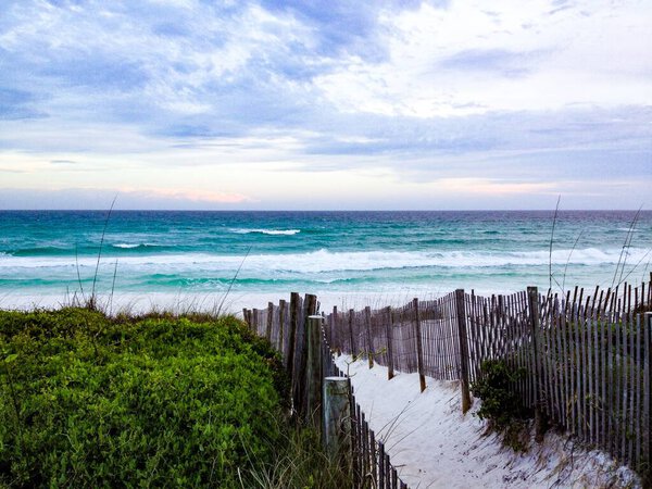 A fenced pathway leading to the beach with splashing sea waves