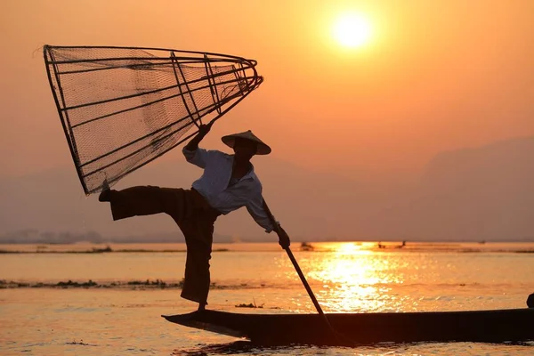 日没時に手作り網で伝統的な方法で魚をキャッチ湖の近くの漁師のシルエット ロイヤリティフリーのストック写真
