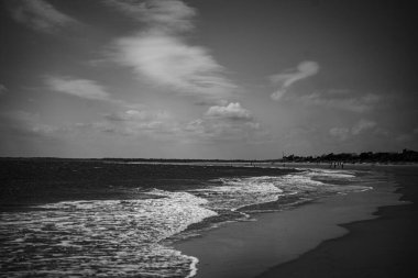 Gri deniz dalgaları kıyıya vuruyor. Arka planda bulutlu bir gökyüzü var.