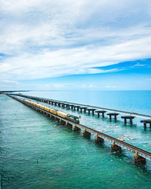 Bir Hint yolcu treni, Pamban köprüsünün üzerinden Arap denizini geçip kısmen bulutlu gökyüzünün altından geçiyor.
