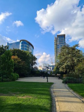 Arka planda modern bina olan yeşil parktaki bir geçidin dikey görüntüsü.