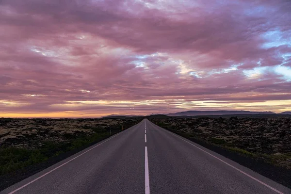 緑に囲まれた空のアスファルトの道の上に美しいピンクの夕日 — ストック写真