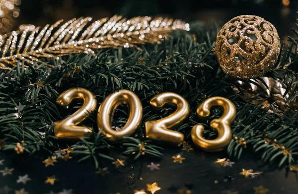 2023年の黄金の数字と装飾のクローズアップ静止画 濃い緑色の松の枝に金の泡と装飾 — ストック写真