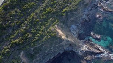 Kıyıdaki yemyeşil bitki örtüsü ve kayalık uçurumlarla çevrili otobanın üzerinde uçan bir insansız hava aracı.