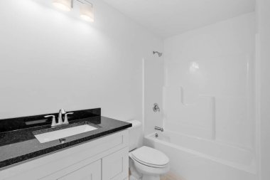 Banyosu ve mermer lavabosu olan beyaz, modern bir tuvalet.