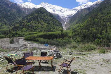 Çimlerin üzerinde bir masa ve sandalyeler ormanlı tepeler ve karlı dağlar berrak arka plan