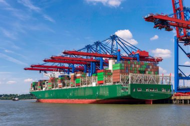 Hamburg konteynır limanında güneşli bir günde büyük bir konteyner gemisi yükleniyor.
