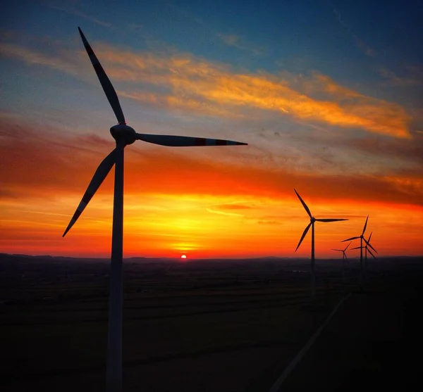 在漆黑的橙色云彩落日的天空背景下 一个令人叹为观止的风力涡轮机在田野里旋转的景象 — 图库照片