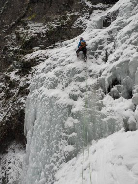 Soğuk bir kış gününde, İtalyan karlı Dolomitlerinde donmuş şelale boyunca tırmanan bir dağcı.